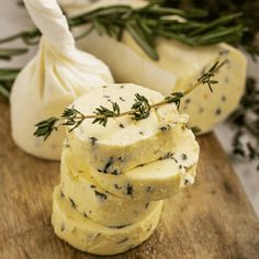 several pieces of cheese sitting on top of a wooden cutting board next to garlic and herbs