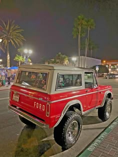 an old red ford bronco is parked on the side of the road at night