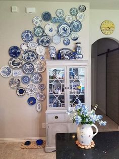 a vase filled with blue and white flowers next to a wall covered in plates on it