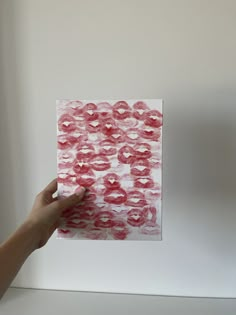 a hand holding up a piece of paper with red paint on it and white background