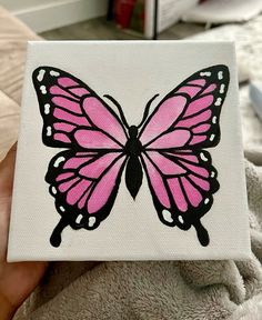 a pink butterfly painted on white canvases with black outline, in someone's hand