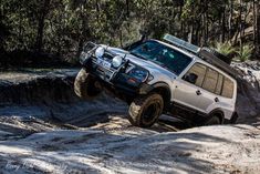 a white four - doored suv is jumping over rocks in the mud with trees behind it