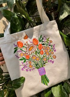 a person holding a white bag with flowers painted on it and butterflies flying over them