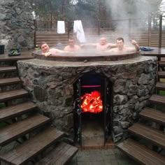 three people in a stone hot tub with wood steps leading up to the fire place