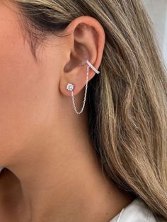 a woman wearing a pair of silver ear cuffs with cubicles on each end and a chain attached to the back of her ear