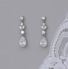 two pairs of diamond earrings on top of a lace doily with an image of the bride's wedding dress in the background