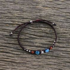 a beaded bracelet with beads and stones on top of a wooden table next to a rock