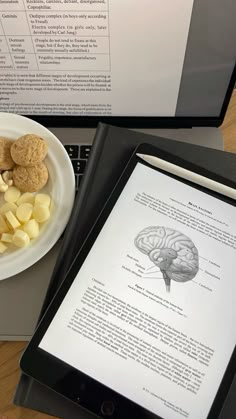 the tablet is next to a bowl of food and a book on top of it