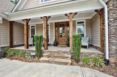 the front porch of a house with stone pillars and wood columns on each side, surrounded by greenery