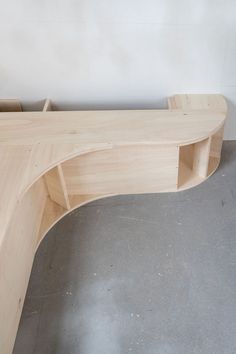 a curved wooden bench sitting on top of a cement floor next to a white wall