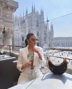 a woman sitting at an outdoor table with a purse and wine glass in her hand