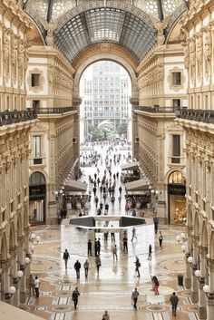 people are walking around in the middle of an indoor shopping mall with high ceilings and arched windows