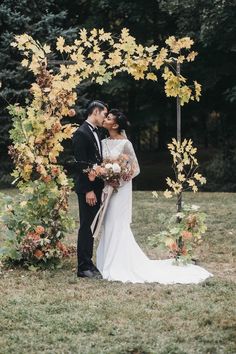 a bride and groom kissing under an arch decorated with autumn leaves at the end of their wedding day