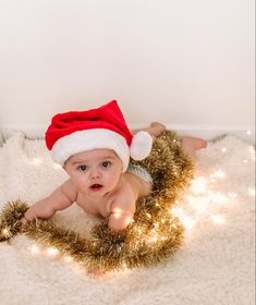 a baby wearing a santa hat laying on top of a white rug next to a christmas wreath