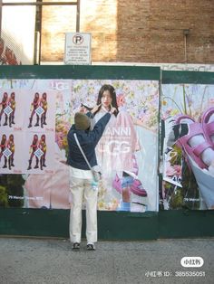 a woman taking a photo of a poster on the side of a building