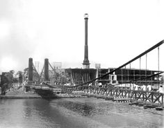 an old black and white photo of a factory with workers on the bridge over water