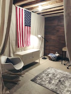 an american flag is hanging in the corner of a room with white drapes on the walls