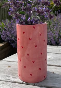 a pink vase filled with purple flowers on top of a wooden table next to lavender plants