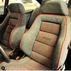 two seats in the back of a car with orange stitching on them and one has a steering wheel