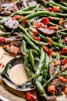 green beans, mushrooms and bacon are on a serving platter with a spoon in it