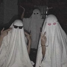 three people in white ghost costumes with their hands up to the camera and one person wearing sunglasses