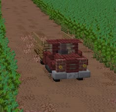 a red truck driving down a dirt road next to a field filled with green plants