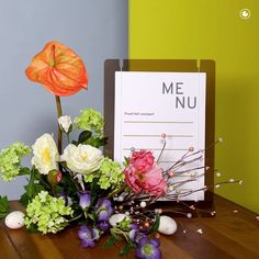 a bouquet of flowers sitting on top of a wooden table next to a sign that says meu