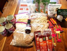 an assortment of food and drinks on a wooden table next to bags of rice, beans, cornflakes, carrots, eggs, and other foodstuffs