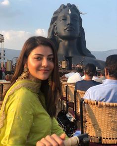 a woman standing in front of a statue with people sitting around her and looking at the camera