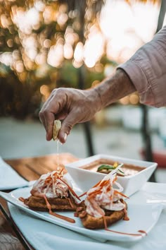 a person is dipping some food into a small bowl on a white plate at an outdoor table