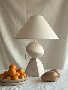 a table lamp sitting on top of a white table next to oranges and bread