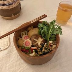 a wooden bowl filled with food next to a glass of beer on a white table cloth