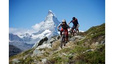 two mountain bikers riding down a trail in front of a snow - capped mountain