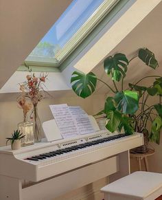 a white piano sitting in front of a window next to a potted plant and vase filled with flowers