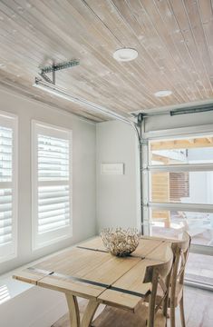 a wooden table and chairs in a room with shutters on the window sill