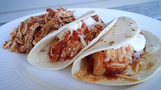 three tacos are sitting on a plate with shredded meat and cole slaw in the background