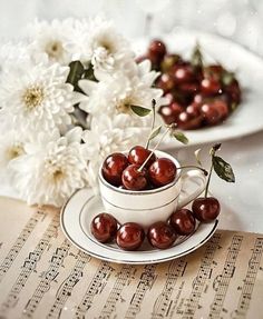 some cherries are sitting in a cup on a table with music sheets and flowers