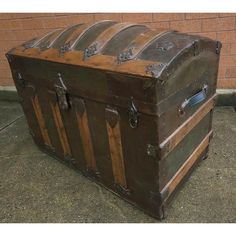 an old trunk is sitting on the ground outside in front of a brick wall,