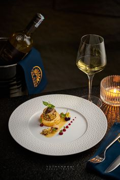 a white plate topped with food on top of a table next to a glass of wine