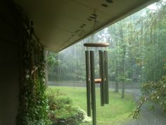 a wind chime hanging from the side of a building next to a forest filled with trees