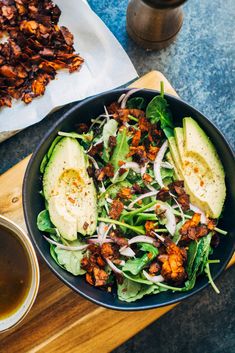 a salad with avocado, bacon and lettuce in a black bowl