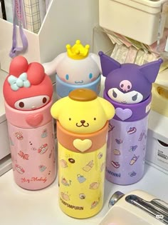 three different colored cups with cartoon characters on them and one has a yellow bow around the top