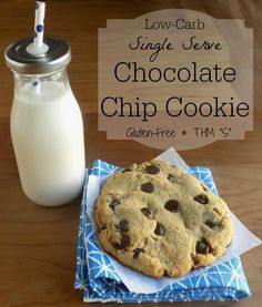 a chocolate chip cookie sitting on top of a blue napkin next to a bottle of milk