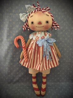 a stuffed doll with a candy cane in its hand on a blue background, wearing a red and white striped dress