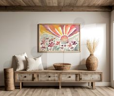 a painting hanging on the wall above a wooden bench with two vases and pillows