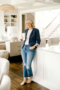 a woman standing next to a kitchen counter holding a coffee cup in her right hand