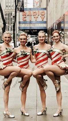 four women in red and white costumes posing for a photo on the sidewalk with their legs wrapped around each other