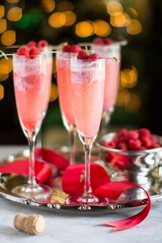 two champagne flutes with raspberries in them on a silver platter and red ribbon