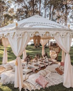 a white canopy bed sitting on top of a lush green park covered in pillows and blankets