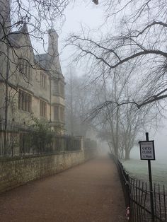 a foggy path leading to an old building with a sign on the fence and trees